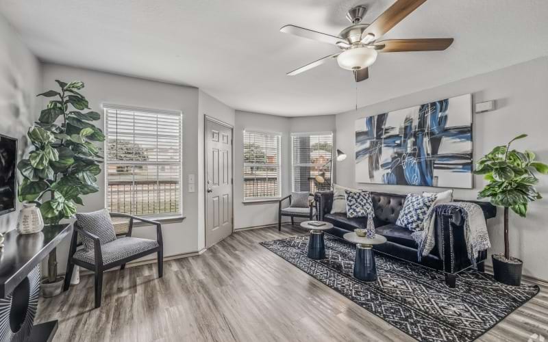 Renovated apartment living room with modern flooring, large windows, ceiling fan, comfortable seating, and contemporary finishes at Fifteen12.